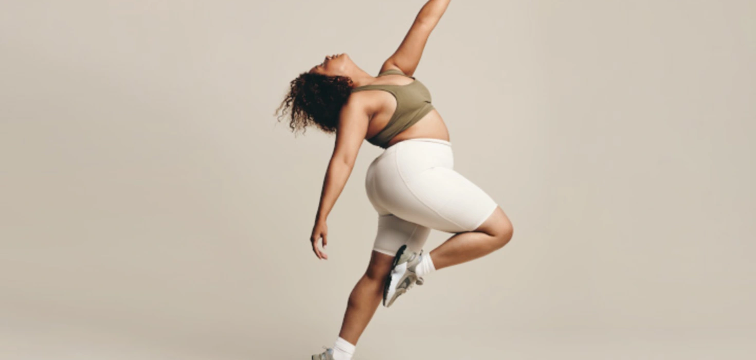 Tanzende Frau in weißer Hose und braunem Top vor einheitlichem Hintergrund