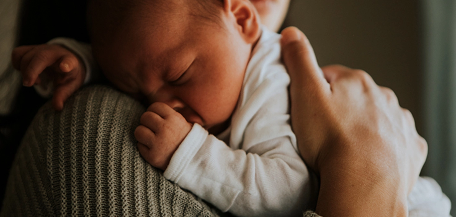Baby liegt auf der Schulter eines Erwachsenen
